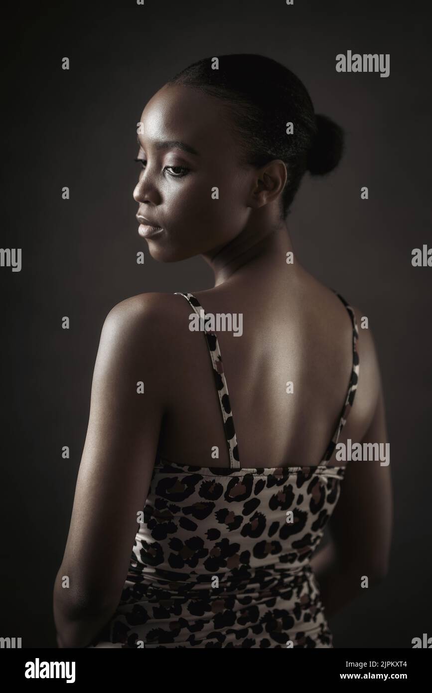 Junge Frau mit dunkler Haut posiert vor dunklem Hintergrund und schaut auf einen Punkt. Hochwertige Fotos Stockfoto