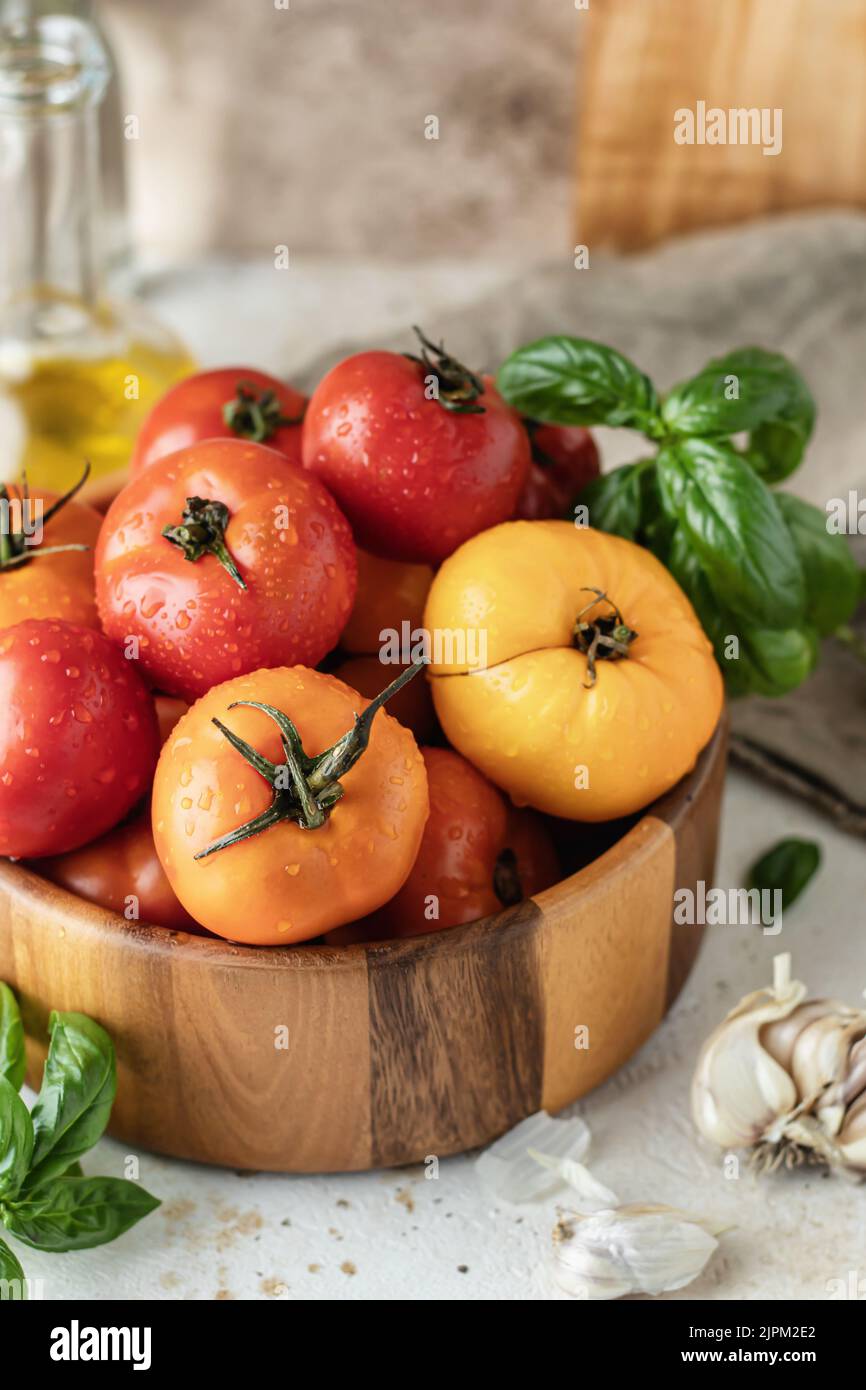 Holzschüssel mit frischen bunten Tomaten, Knoblauch, Basilikum, Pfeffer und Olivenöl auf strukturiertem Hintergrund. Küche Stillleben im rustikalen Stil Stockfoto