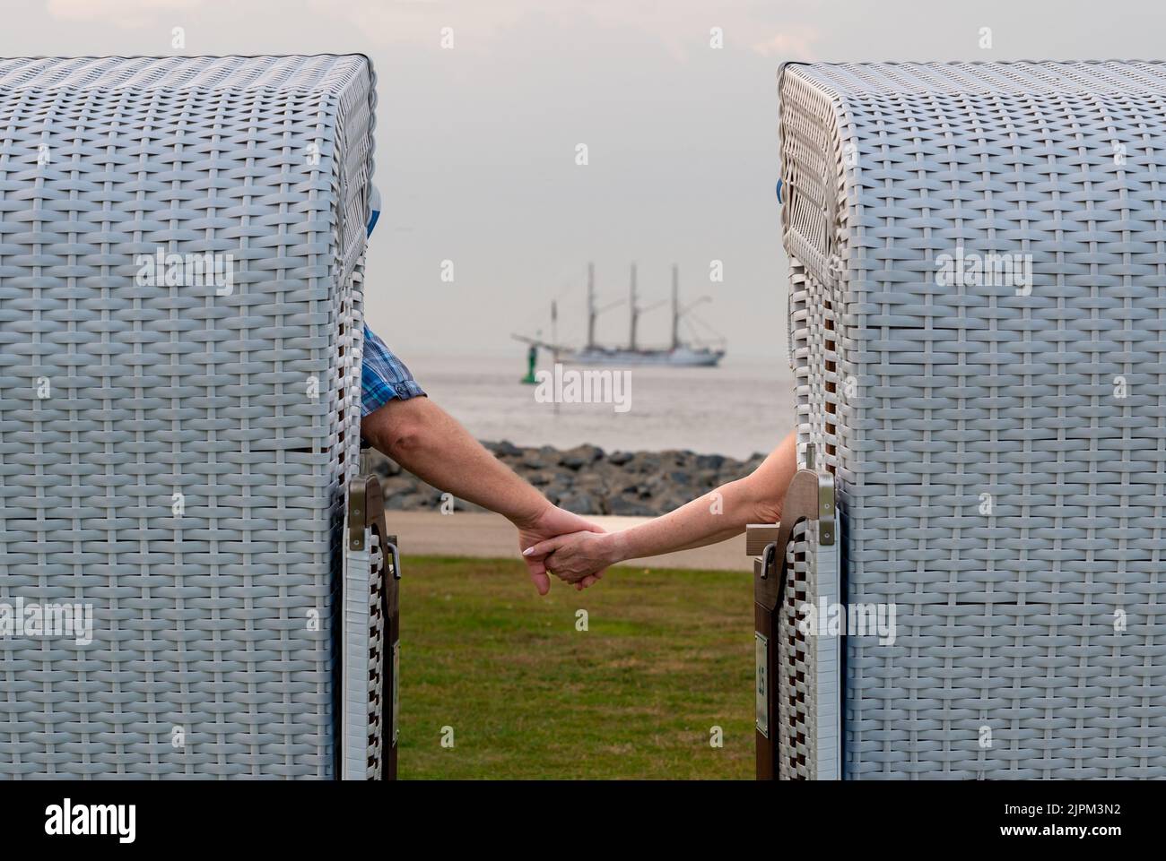 Ein älteres Paar hält sich die Hände, während es in Cuxhaven, Deutschland, auf Liegestühlen sitzt. Stockfoto