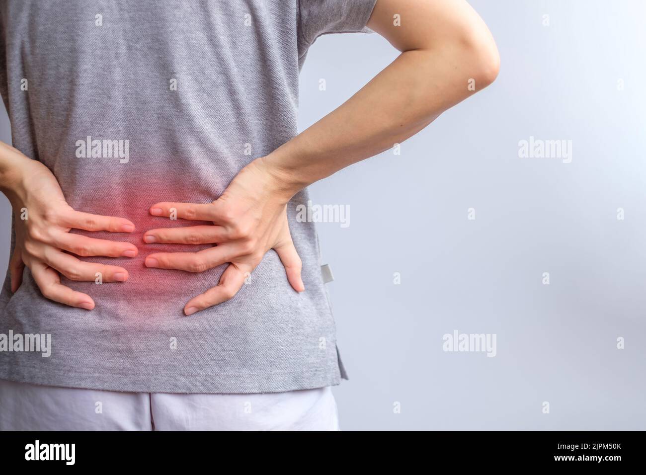 Erwachsene Frau mit Muskelschmerzen auf grauem Hintergrund. Ältere Frau mit Rückenschmerzen aufgrund des Piriformis-Syndroms, Rückenschmerzen und Spinalkompression Stockfoto