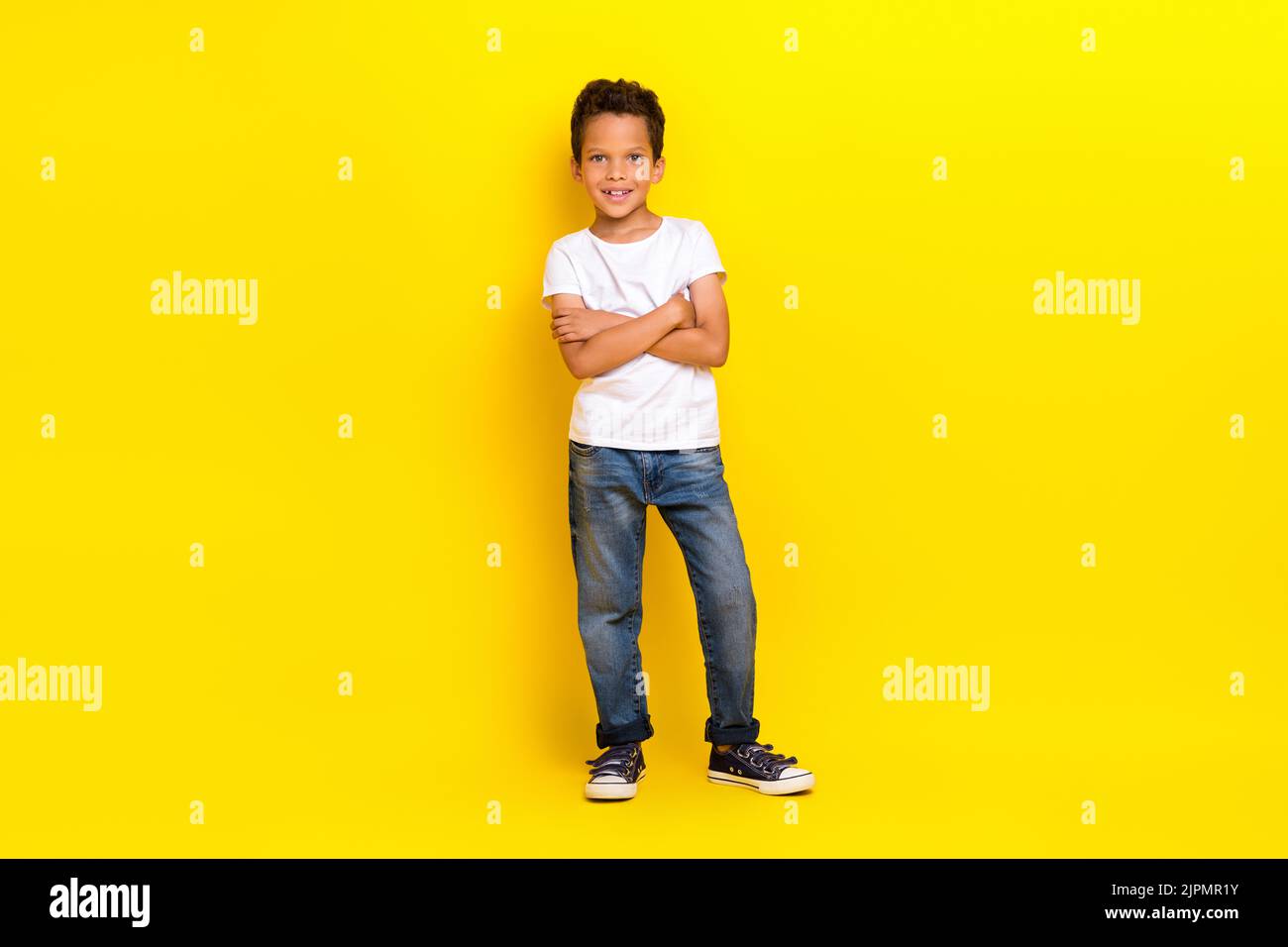 Foto von Boss kleiner Junge gekreuzte Arme tragen weißes T-Shirt Jeans Sneakers isoliert auf gelbem Hintergrund Stockfoto