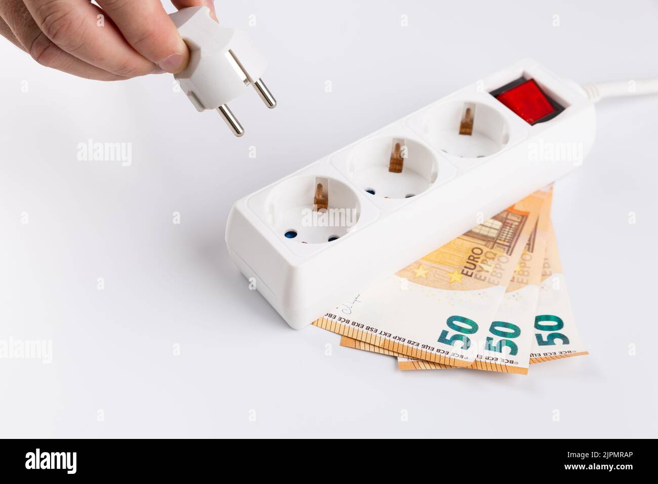 Anonymous Hand steckt ein elektrisches Gerät mit 50 Euro an eine Steckdose. Anstieg der Strompreise Stockfoto