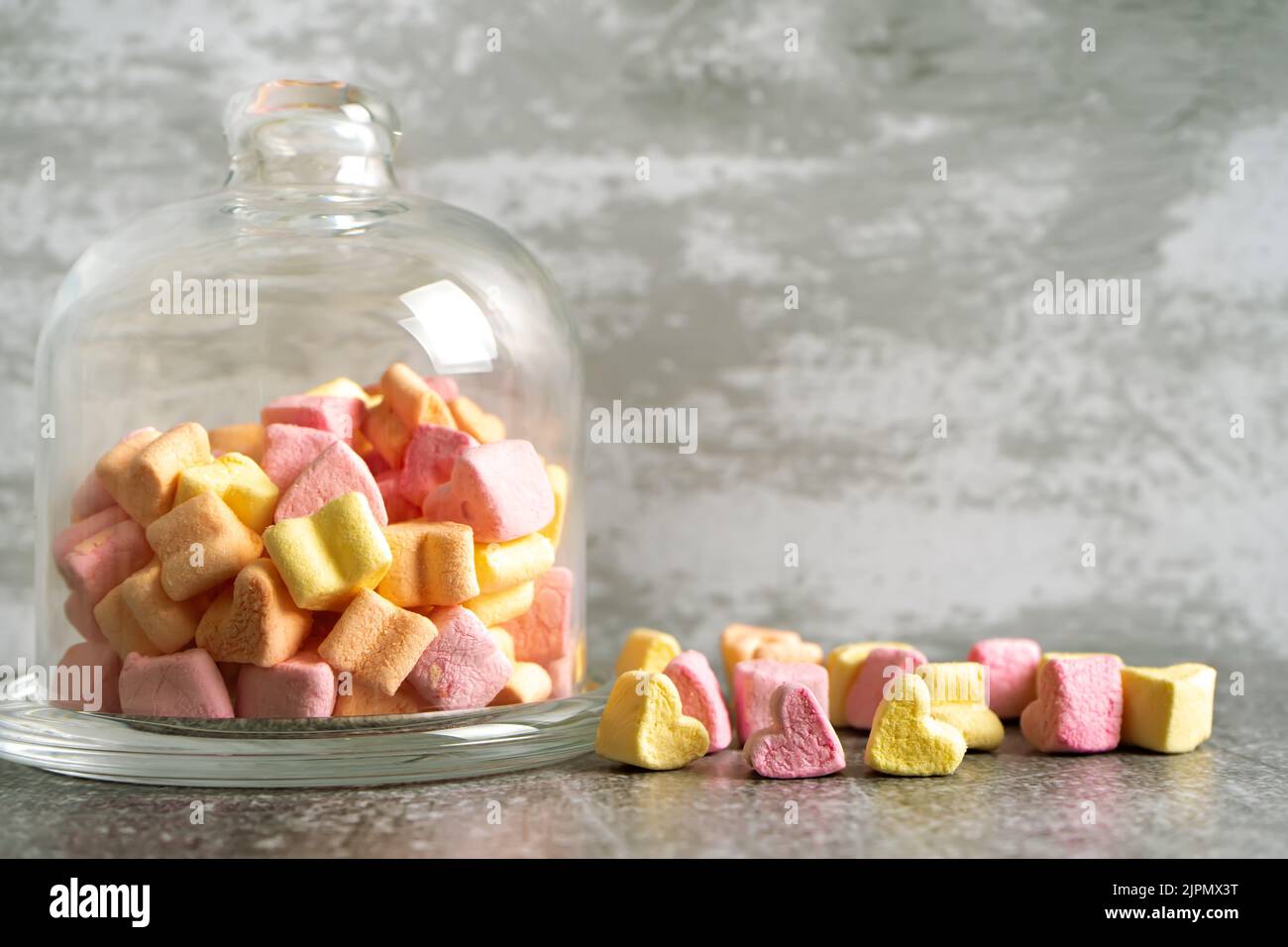 Rosa und gelbe herzförmige Marschall in Glas Glocke auf grauem Beton Hintergrund. Romantisches Dessert im Retro-Pastellstil. Modell, Vorlage w Stockfoto