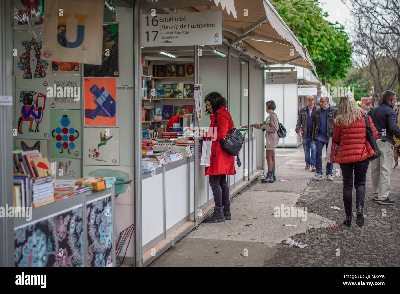 Bild einer in Rot gekleideten Kundin, die an einem Buchladen-Stand auf der Buchmesse im Park um ein Buch bittet, während andere Menschen hinter sich herlaufen Stockfoto