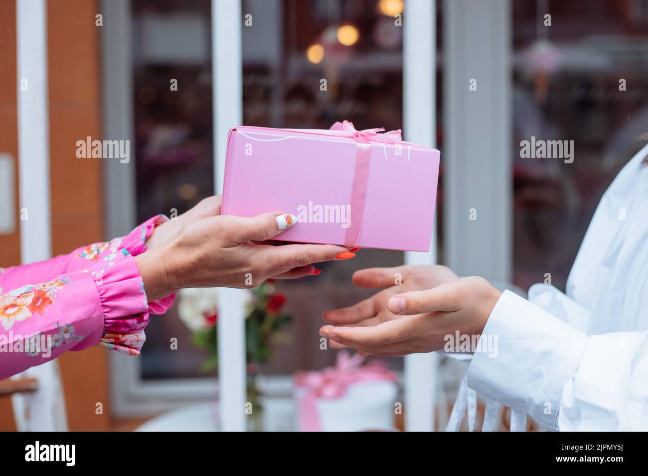 Beschnitten Nahaufnahme Frau Hände mit Maniküre geben Geschenk rosa Box mit Band, Hand in Hand. Geburtstagsfeier Stockfoto