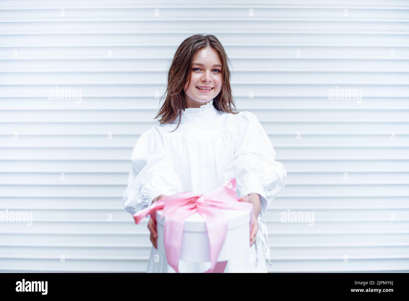 Fröhliche, fröhlich, ziemlich blonde Teenager-Mädchen in weißem Kleid hält rosa Urlaub Geschenk-Box mit Band. Speicherplatz kopieren Stockfoto