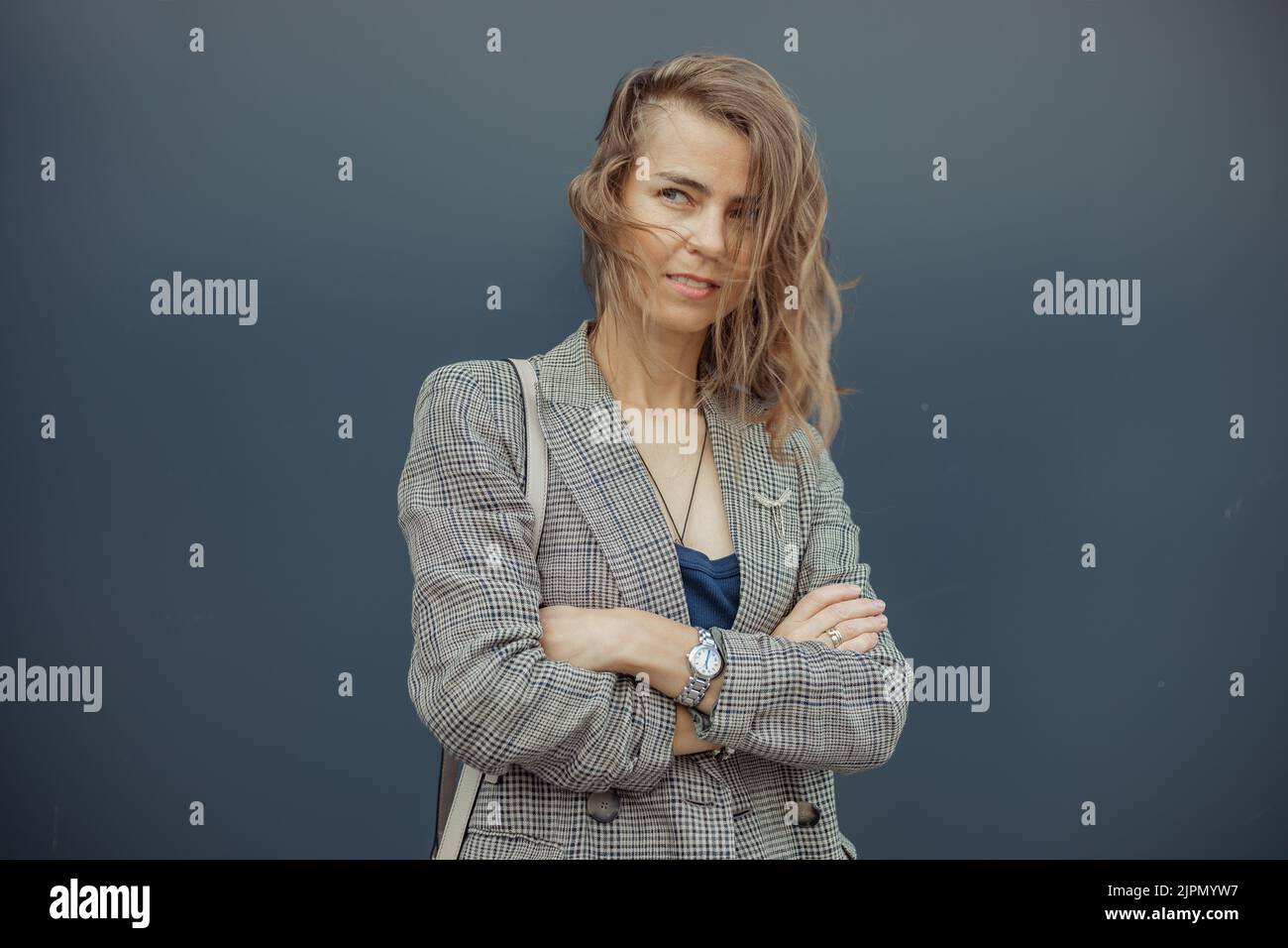 Porträt einer jungen, geheimnisvollen, schlanken Frau mit grünen Augen, die auf blauem Hintergrund mit gekreuzten Händen steht und posiert zur Seite schaut. Stockfoto