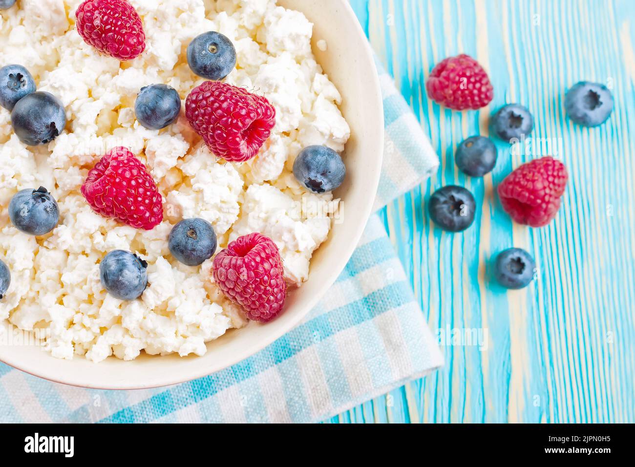 Quark mit Himbeeren und Heidelbeeren in einer Schüssel auf blauem Holzhintergrund. Milchprodukte, gesunde Lebensmittel. Stockfoto