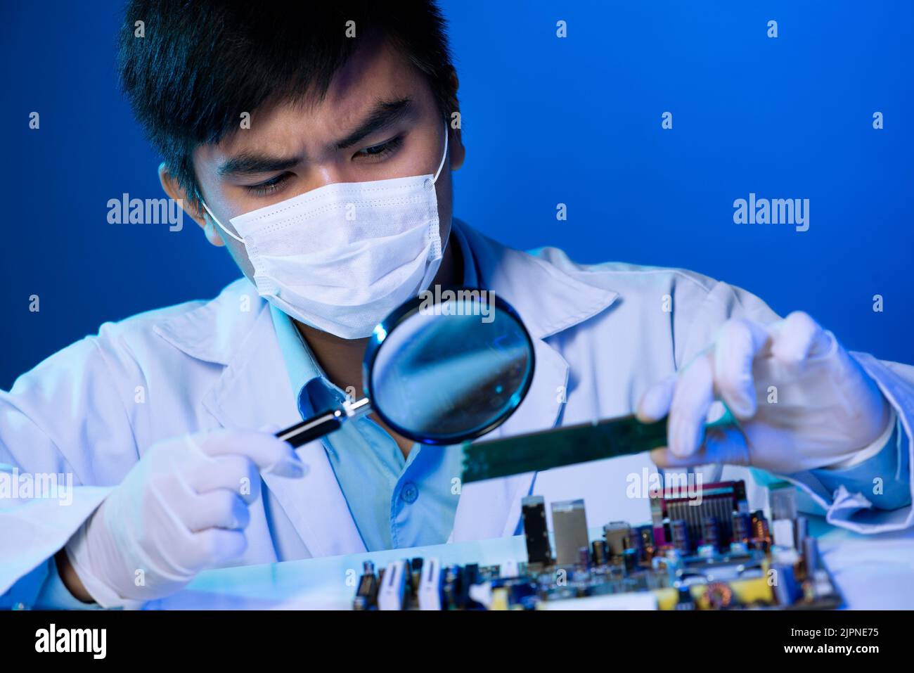 Vietnamesischer Elektronikingenieur schaut durch die Lupe auf das Motherboard Stockfoto