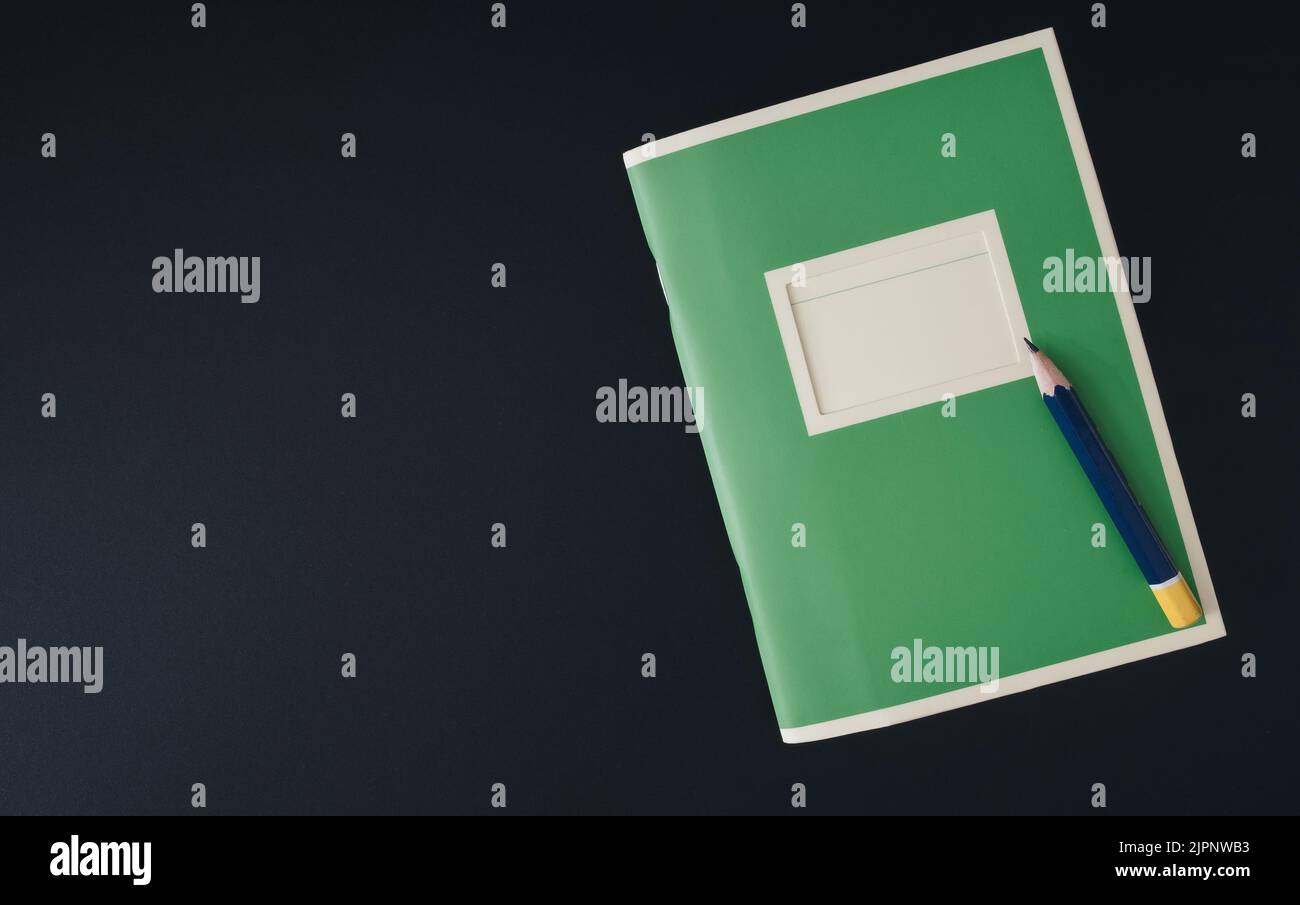 Draufsicht auf ein kleines grünes Notizbuch und einen Bleistiftstumpf auf einem dunklen Tisch Stockfoto