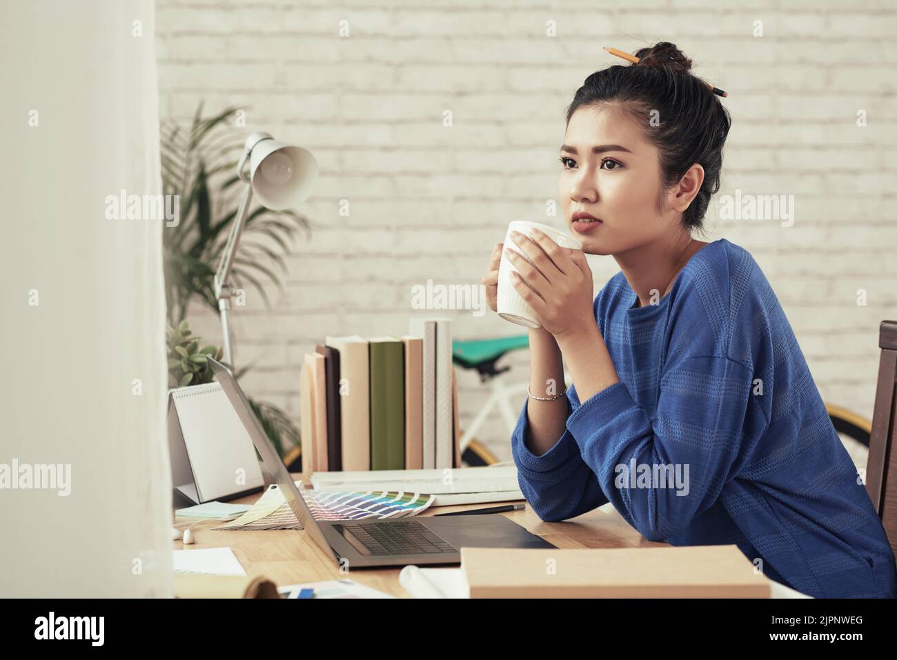 Porträt einer nachdenklichen vietnamesischen Freiberuflerin mit einer Tasse Kaffee an ihrem Tisch Stockfoto