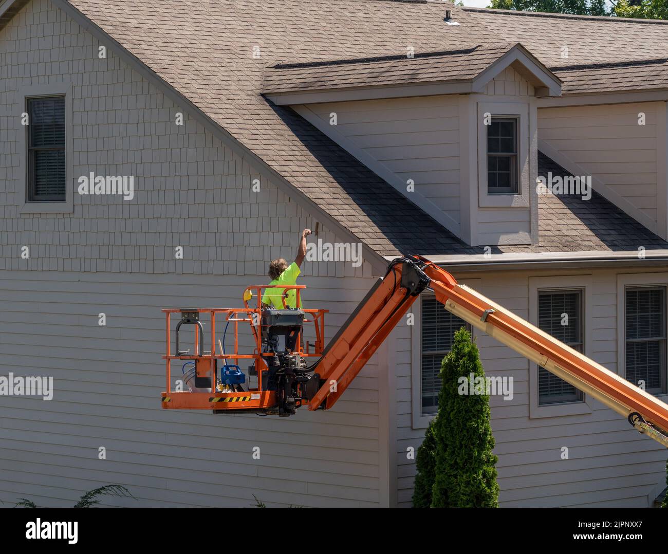 Ein Arbeiter malt die Seite eines Stadthauses, während er in einem Gelenkarm steht Stockfoto