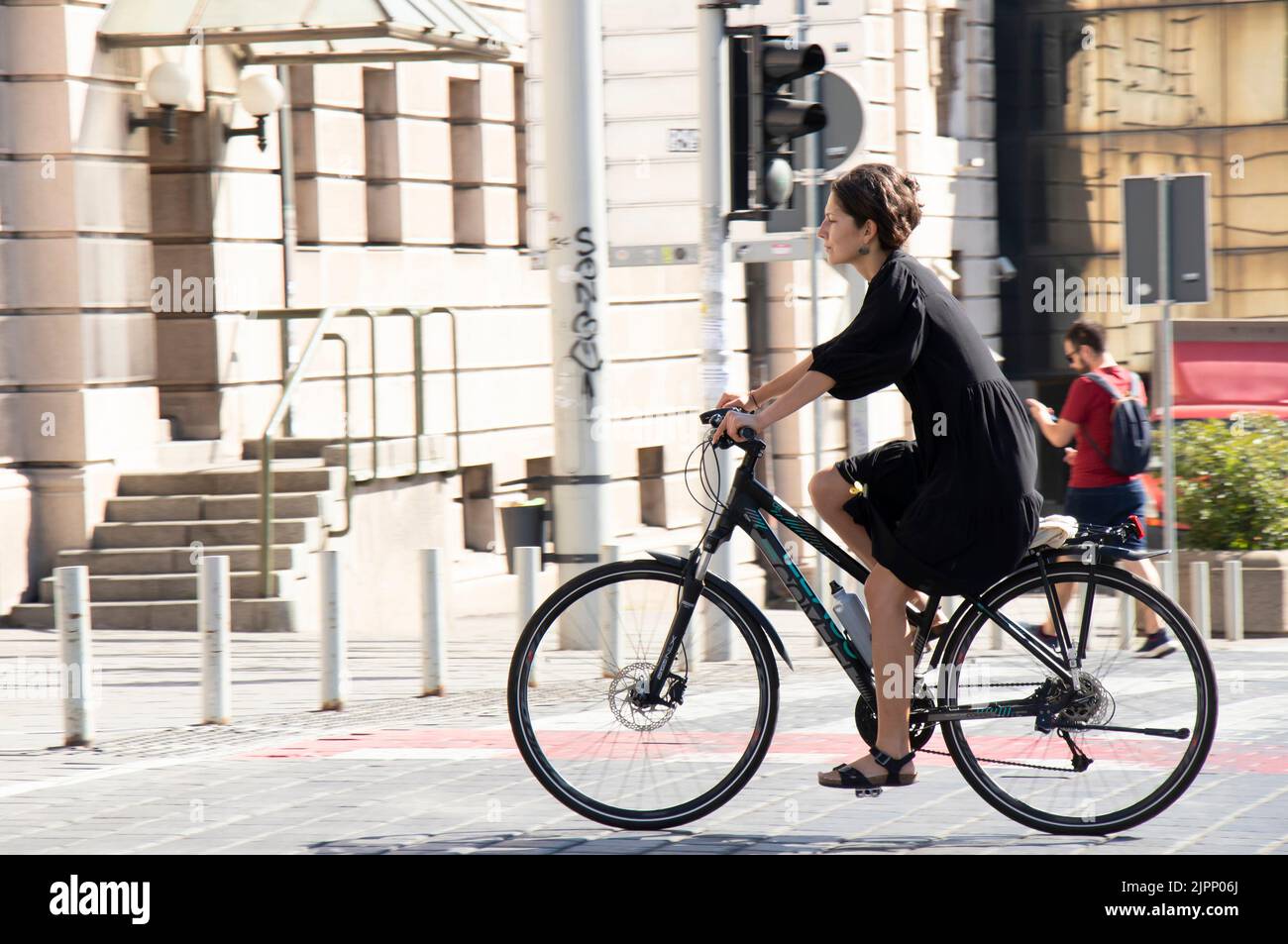 Belgrad-Serbien - 15. Juni 2022: Elegante junge Brünette in schwarzem Kleid auf dem Fahrrad auf der Straße der Stadt Stockfoto