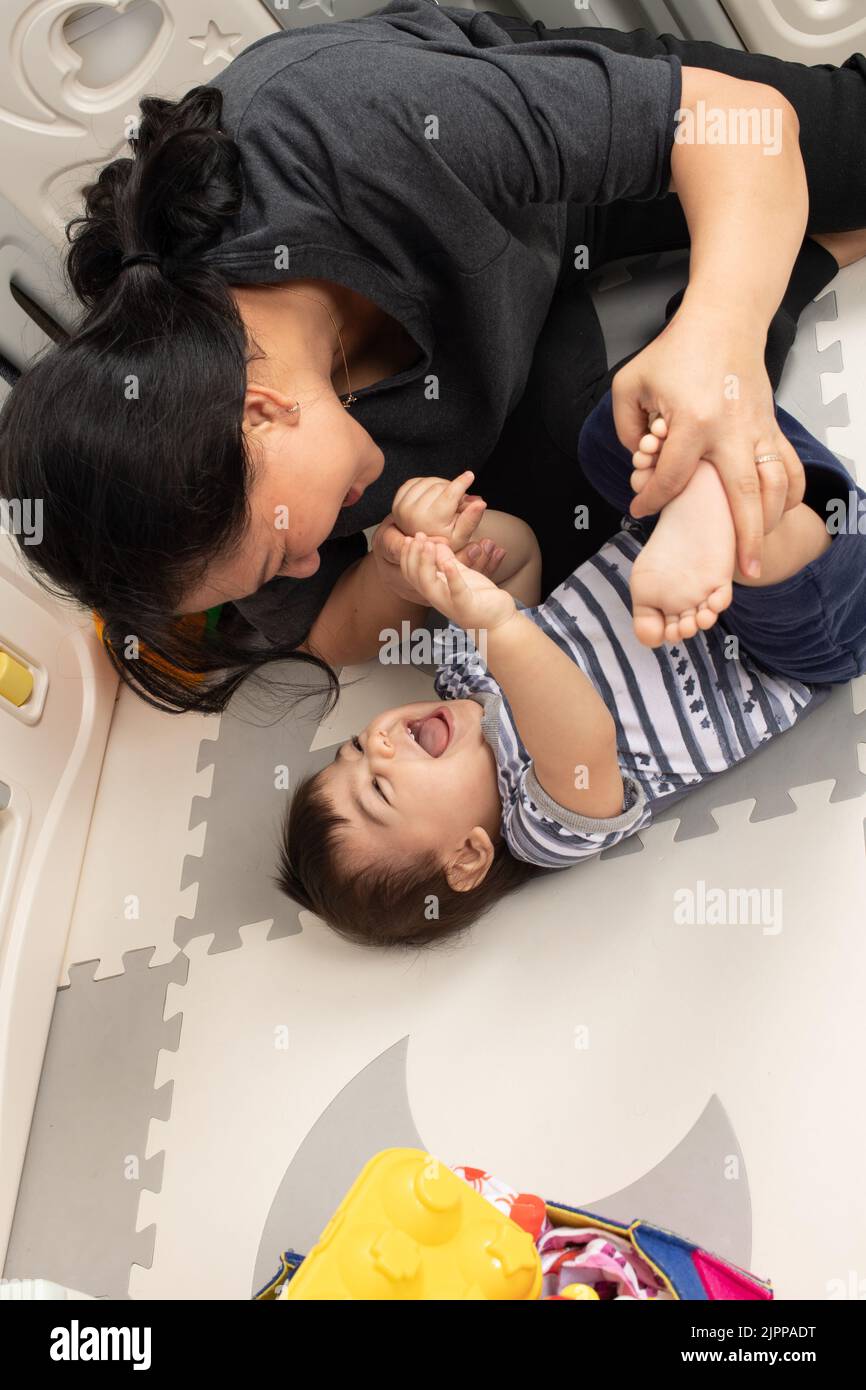 11 Monate alter Junge zu Hause mit Mutter, interagierend, körperliches Spiel, lachend Stockfoto