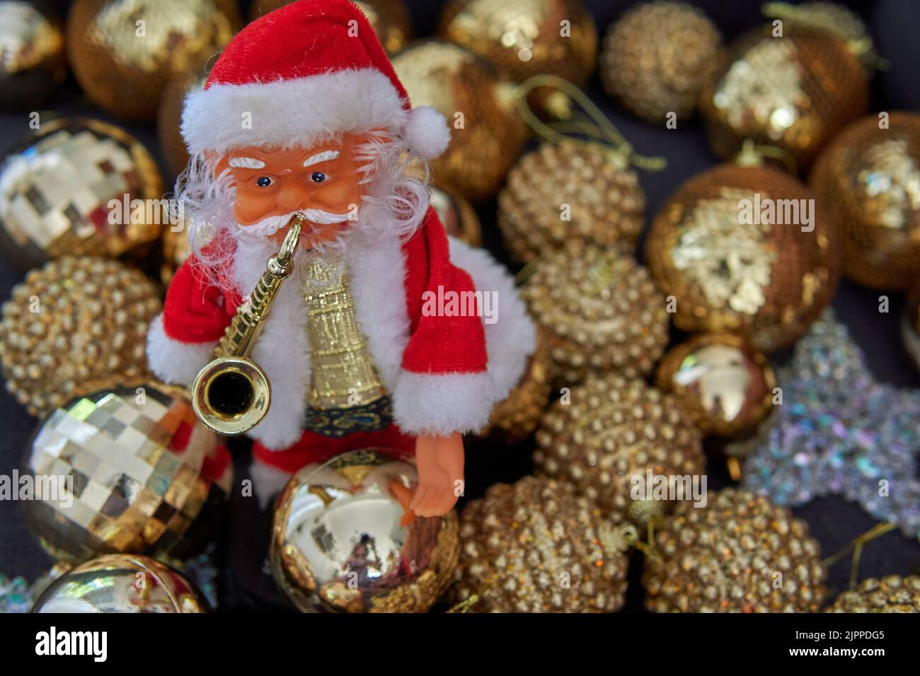 Kleine Puppe vom Weihnachtsmann mit Saxophon auf der Vorderseite mit golden schimmernden Kugeln im Hintergrund. Weihnachtsdekoration Stockfoto