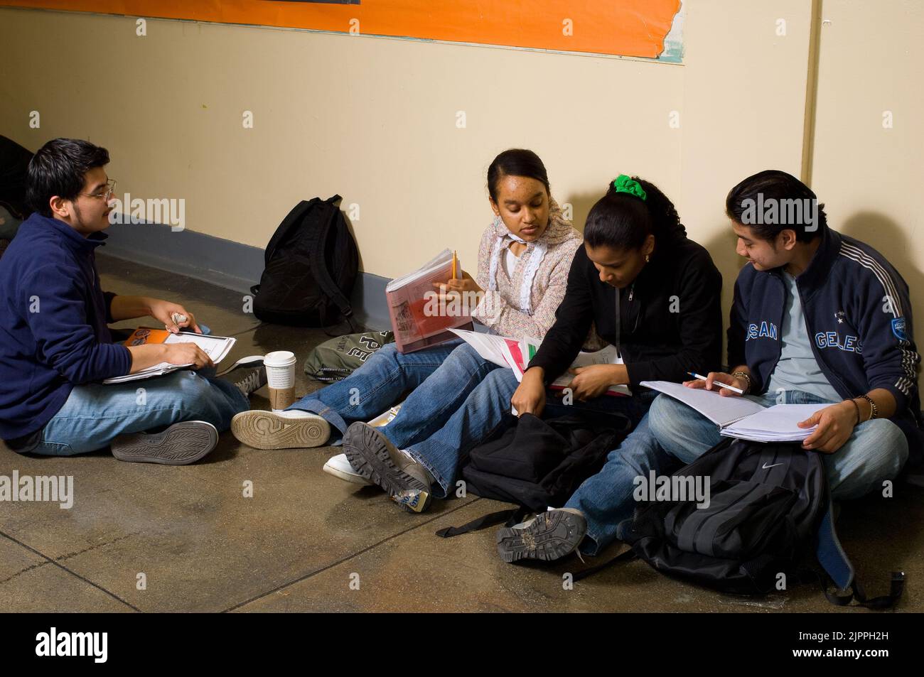 Schülerinnen und Schüler der öffentlichen Schule, die im Korridor zwischen den Klassen sitzen und die Schularbeit betrachten und miteinander sprechen Stockfoto