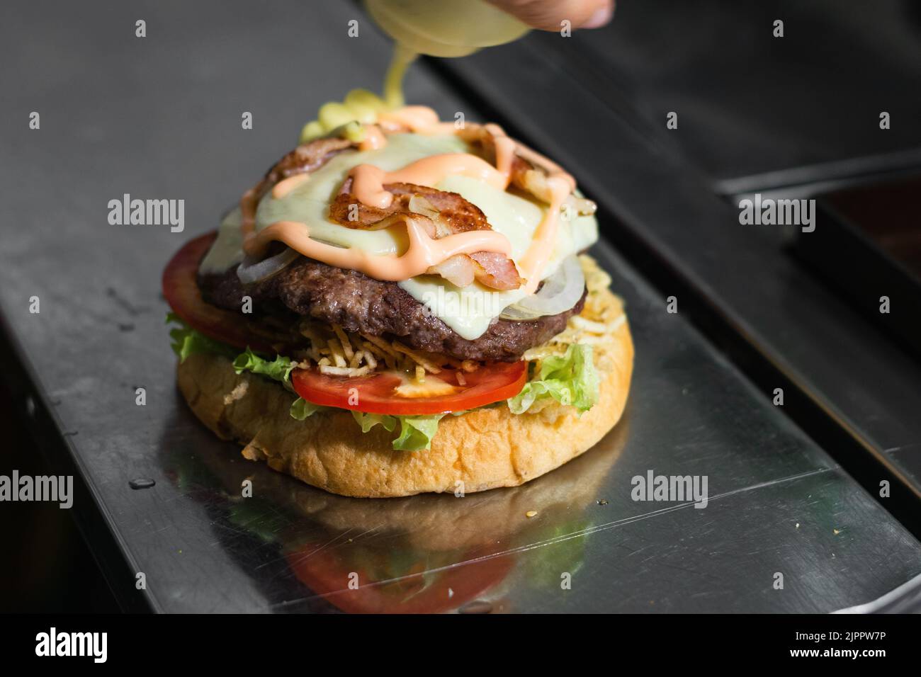 Nahaufnahme der Zubereitung eines kolumbianischen Hamburgers in einem Street Food Stand. Brot, Salat, Tomaten, pommes auf Stöcken, Hamburger-Fleisch, Mozzarell Stockfoto