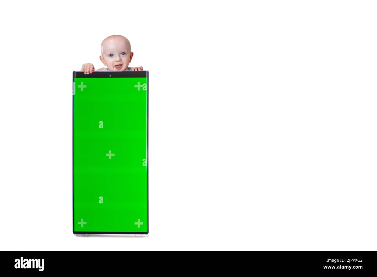 Kleine niedliche Baby guckt aus hinter dem Smartphone mit grünem Bildschirm auf weißem Hintergrund isolieren. Stockfoto