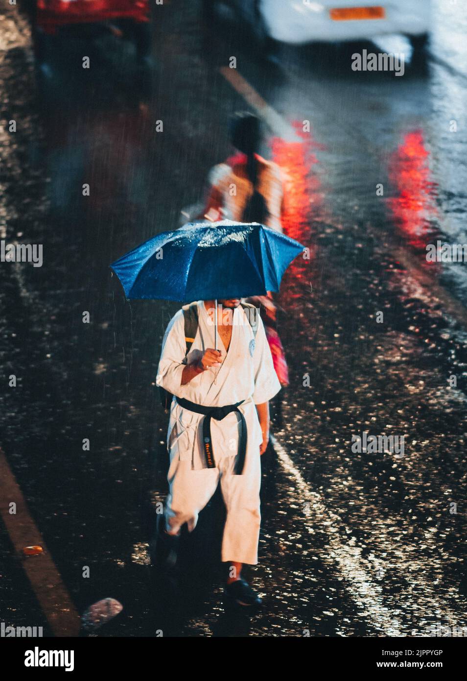 Ein regnerischer Tag in einer Stadt mit einer Nahaufnahme eines Mannes in Sportuniform, der mit blauem Regenschirm unter dem Regen läuft Stockfoto