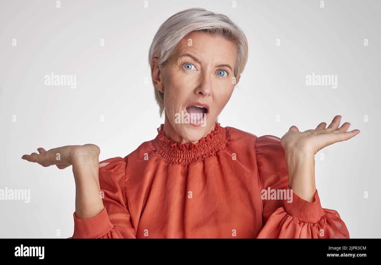 Reife überrascht, wow und schockiert Frau Gesicht vor einem grauen Copy Space grauen Studio Hintergrund posiert mit ihren Händen nach oben und fühlen sich unsicher. Porträt von Stockfoto