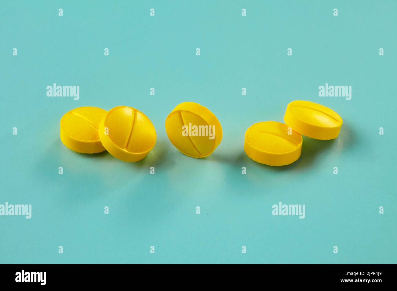 Fünf kleine gelbe Tabletten auf cyanfarbenem Hintergrund Stockfoto