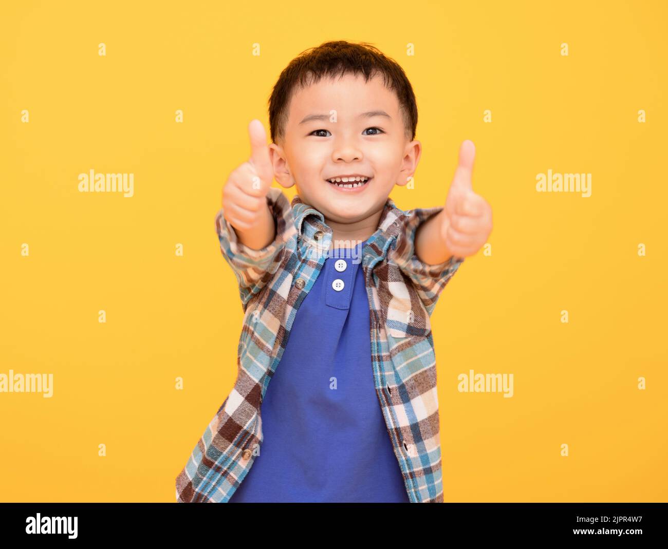 Glücklicher kleiner Junge vor gelbem Hintergrund und zeigt Daumen nach oben Stockfoto