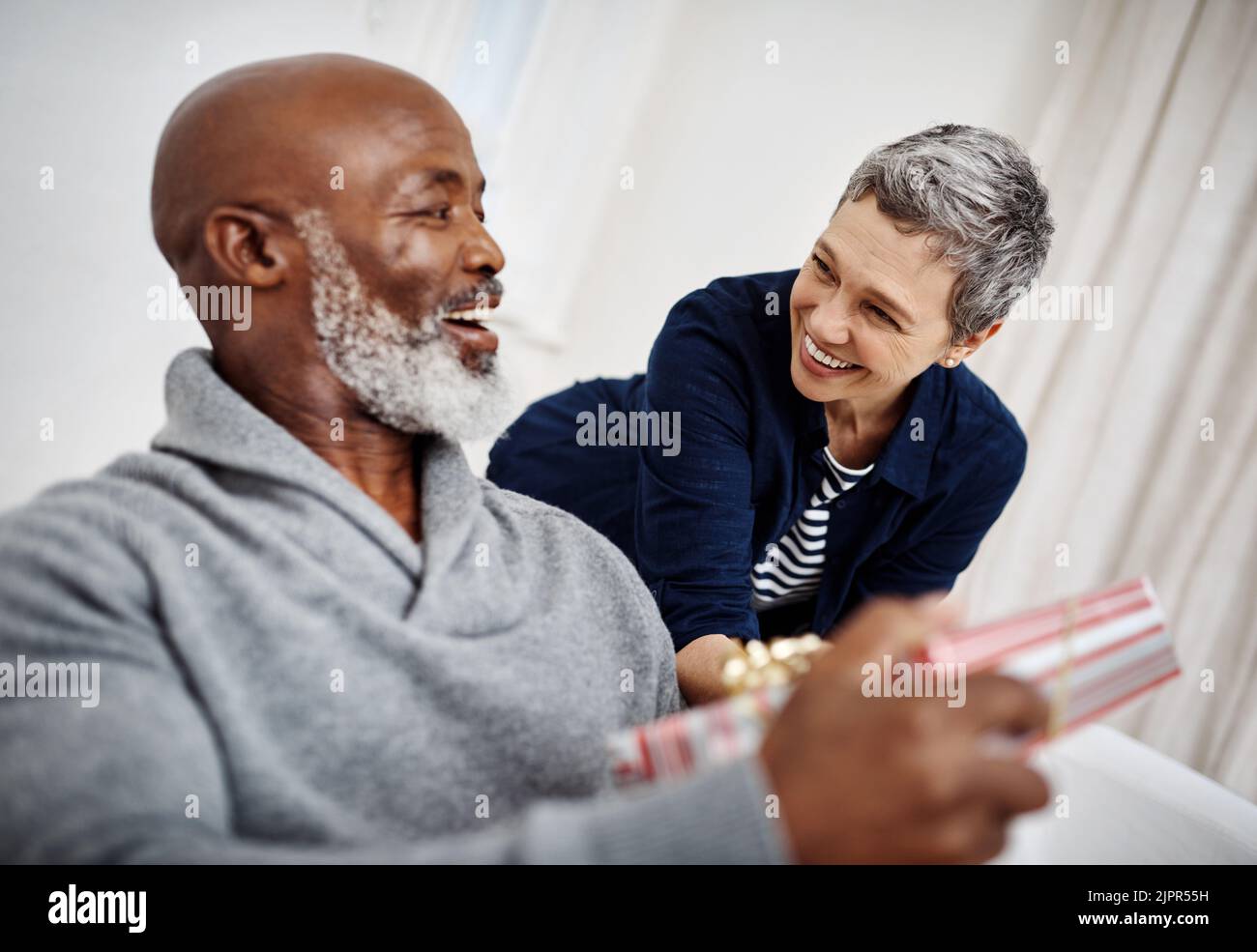 Alles gute zum Jahrestag meiner Liebe. Eine attraktive ältere Frau überraschte ihren Mann mit einem Geschenk zu Hause. Stockfoto