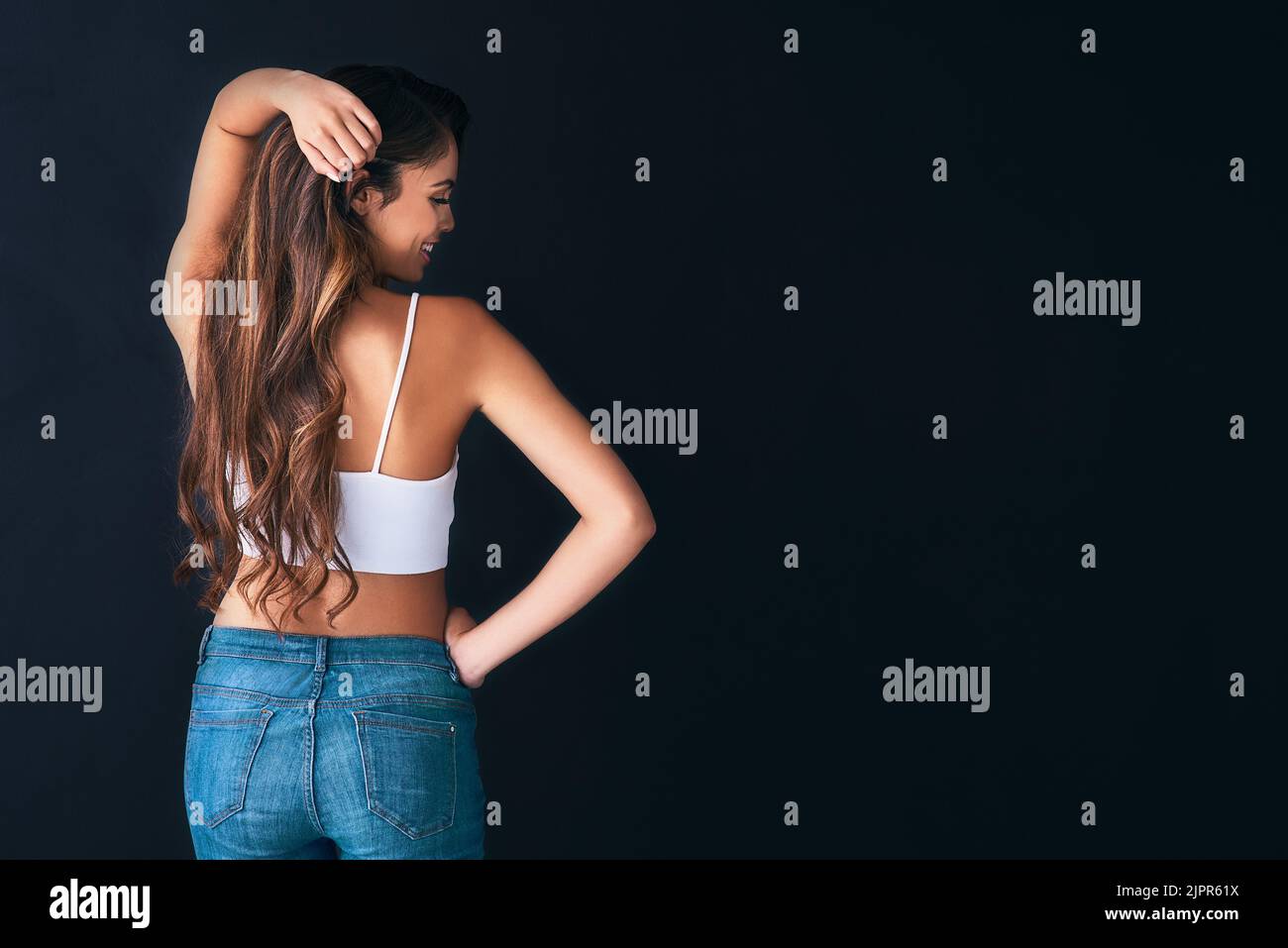 Ich kann einfach nicht aufhören, mein voluminöses, gesundes Haar zu berühren. Studioaufnahme einer attraktiven jungen Frau, die vor dunklem Hintergrund posiert. Stockfoto