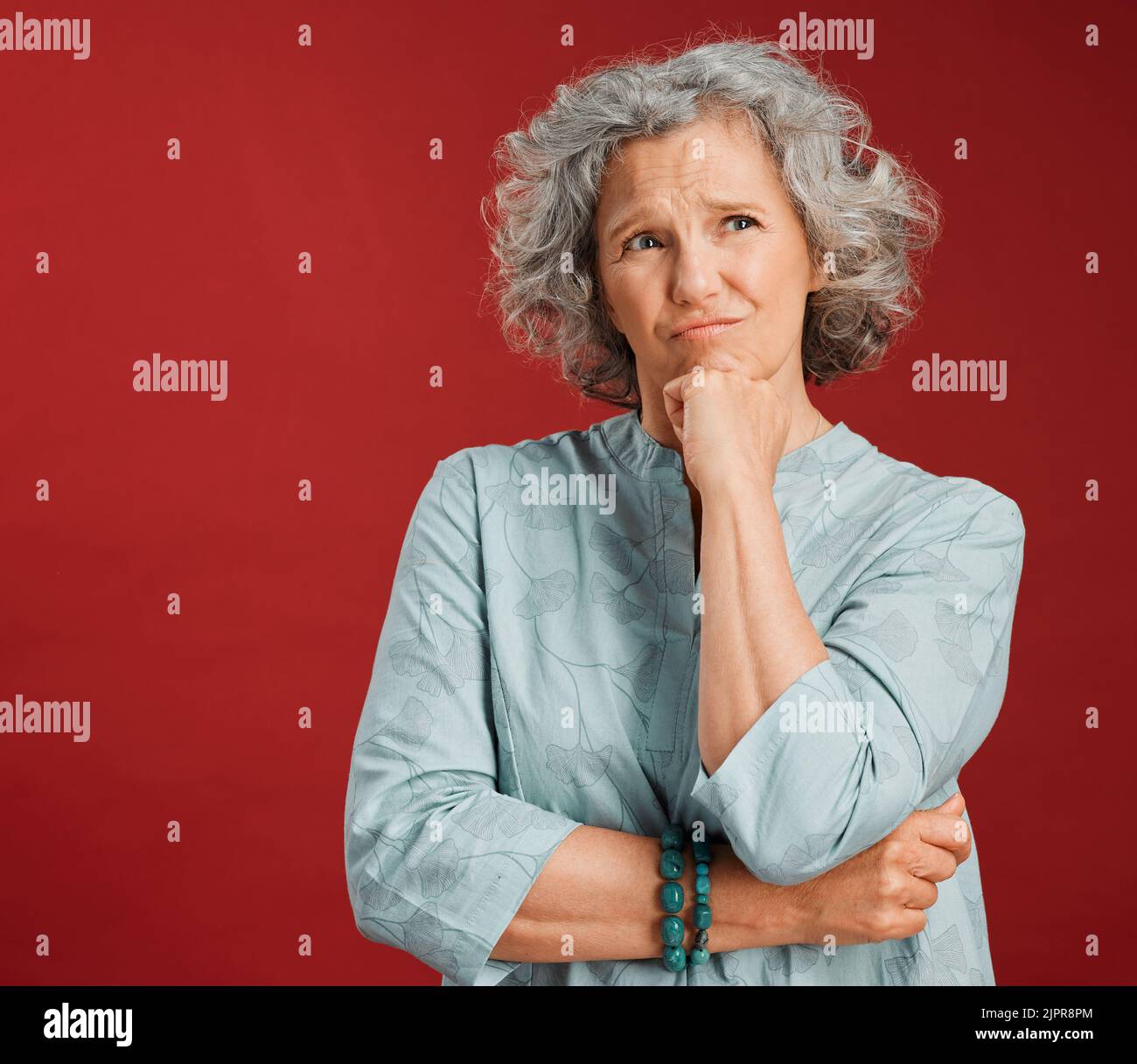 Denkende, verwirrte und wundernde Frau, die verwirrt, unsicher und unsicher über Wahl, Entscheidung und Idee vor dem Hintergrund des Studio-roten Hintergrunds aussahen Stockfoto