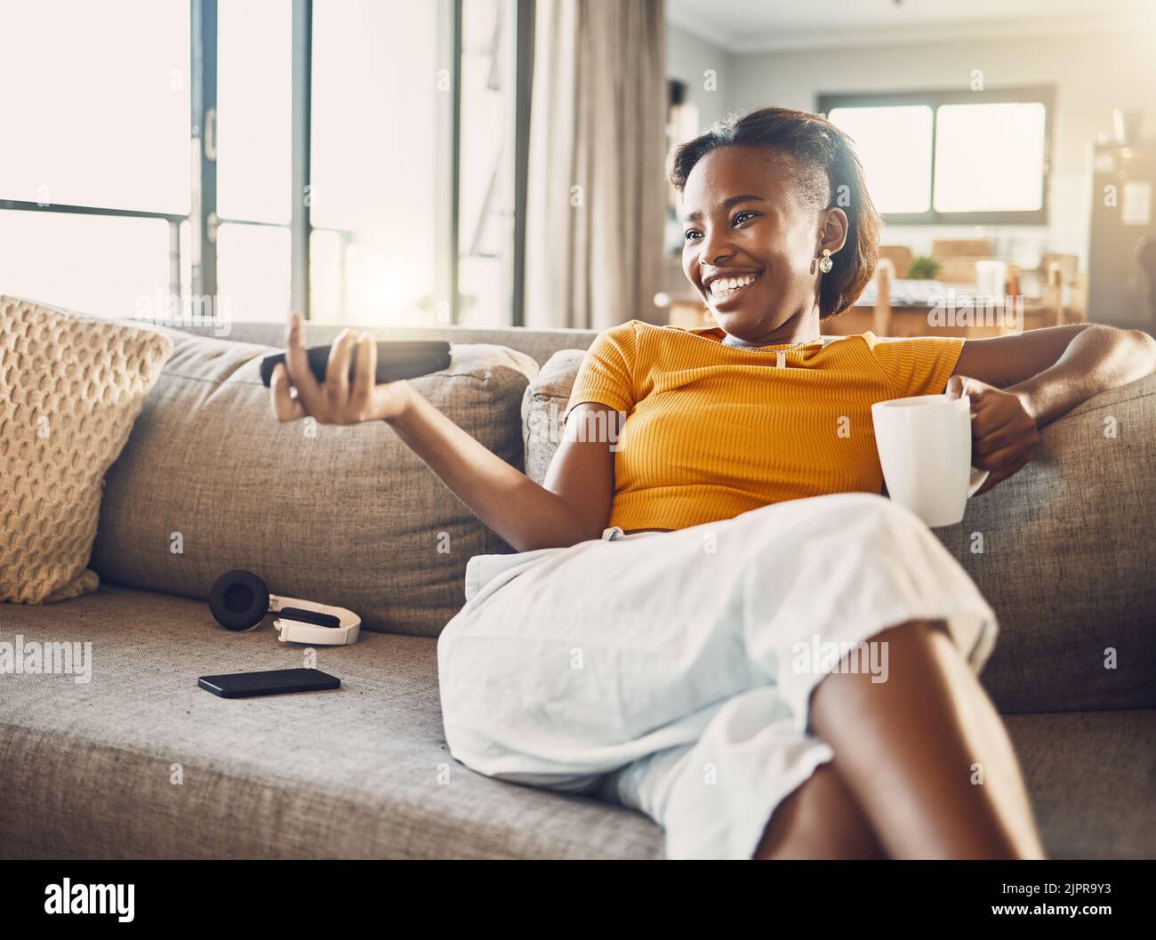 Entspannt, sorglos und lächelnd sieht die junge Frau zu Hause Fernsehen und Filme streamen auf ihrem Sofa im Wohnzimmer. Glückliche, lässige und bequeme Frau Stockfoto
