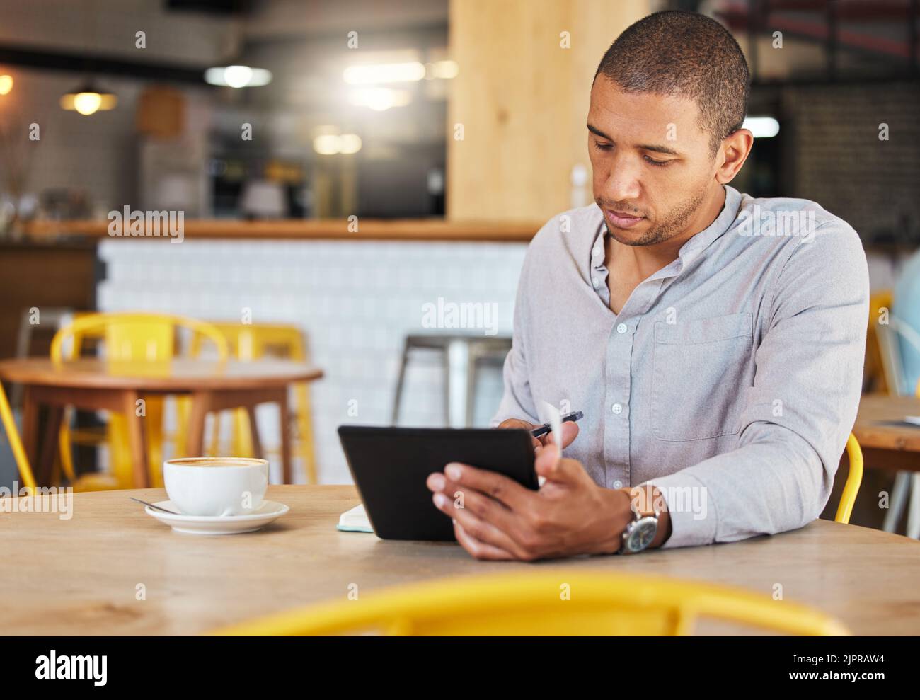 Seriöser freiberuflicher Geschäftsmann, der in einem Café arbeitet und für sein Startup Remote-Unternehmen arbeitet. Junger männlicher Unternehmer mit einer Tablette, die Wachstum plant Stockfoto