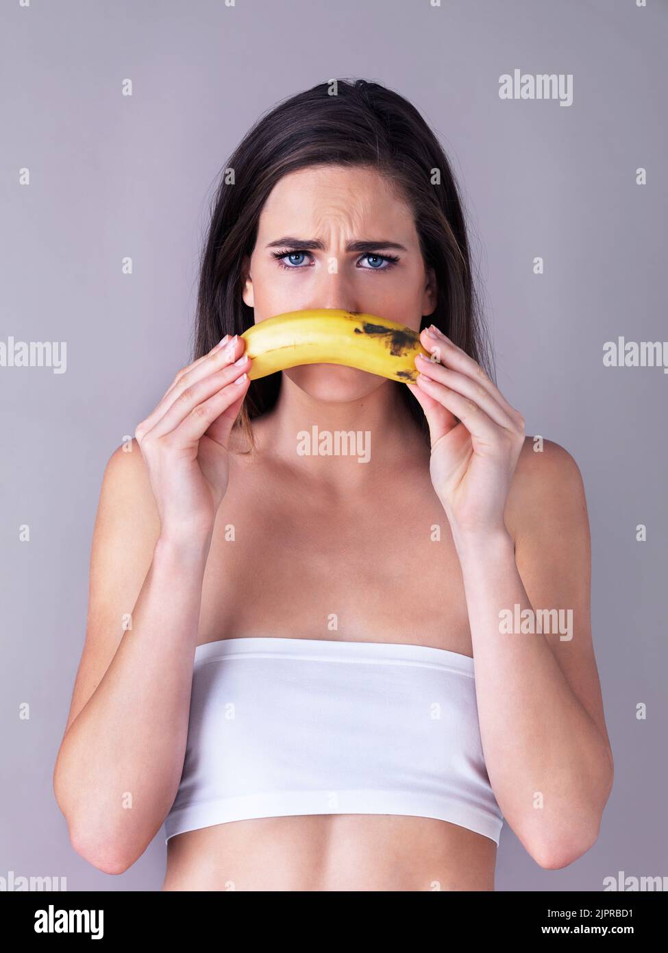 Shes ein trauriger Affe...Studioportrait einer attraktiven jungen Frau, die eine Banane vor einem violetten Hintergrund hält. Stockfoto