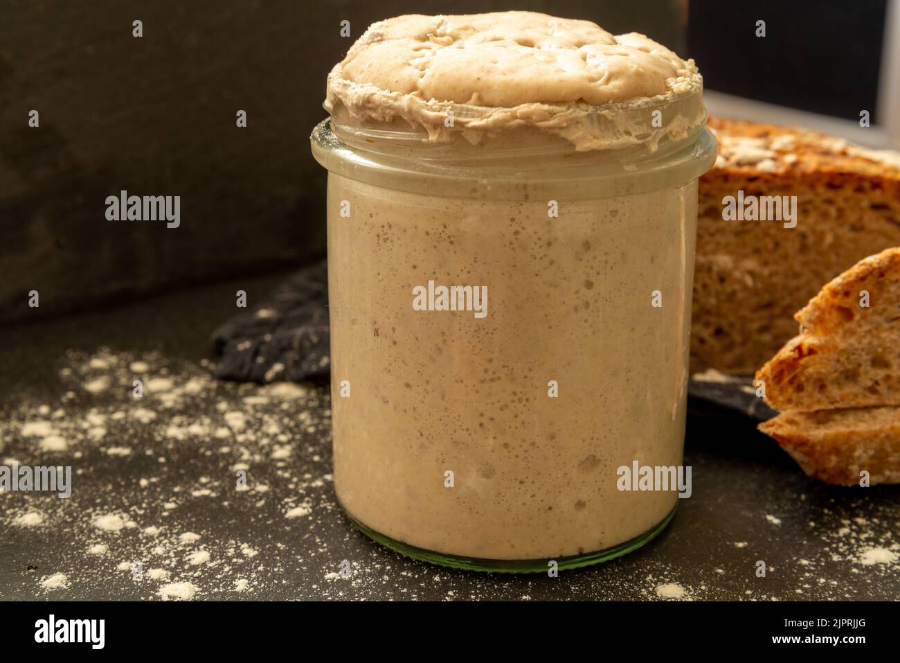 Selbstgemachter Sauerteig-Starter in Glas auf dunklem Hintergrund und graham-Brot Stockfoto