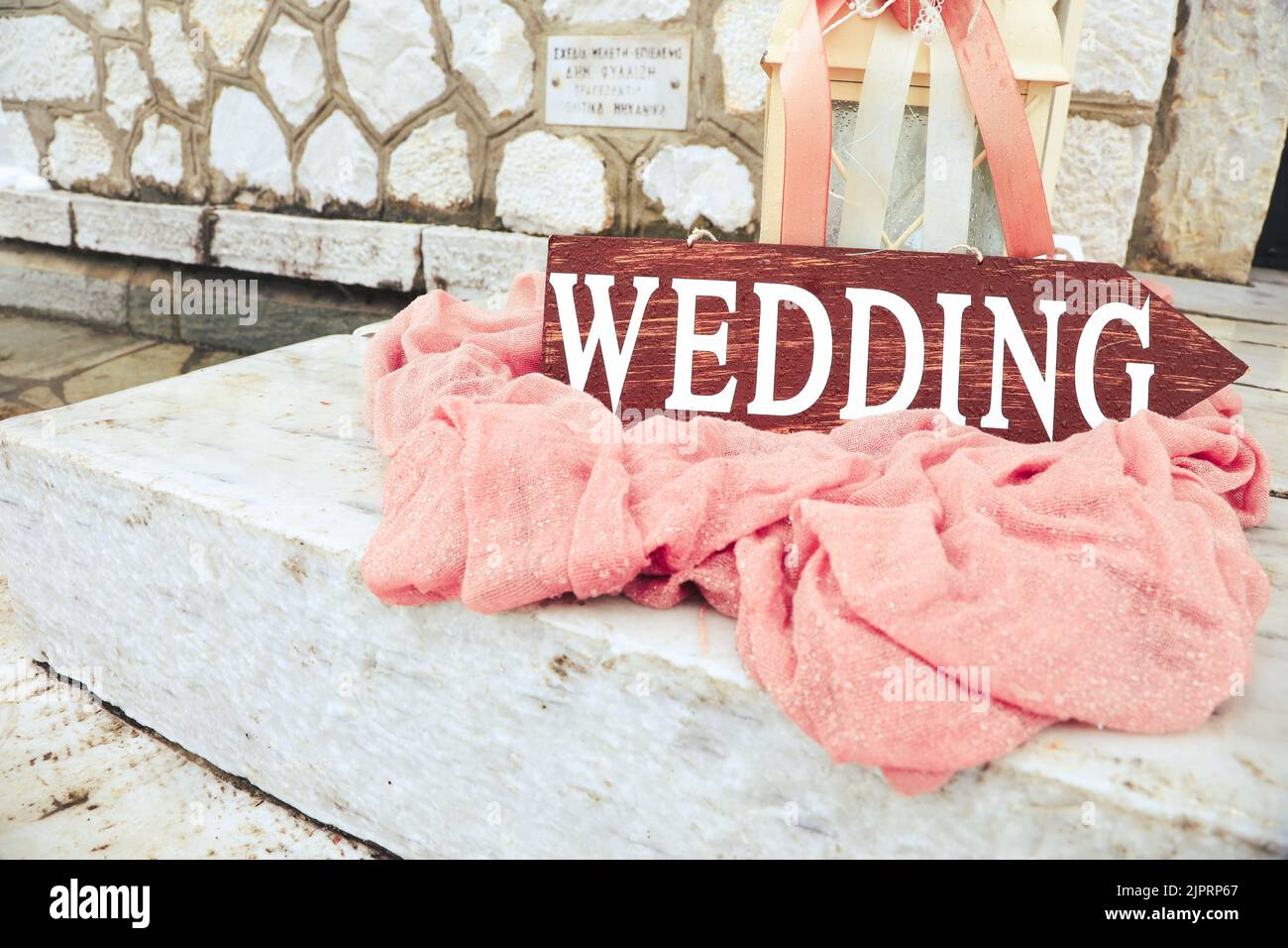Schöne Hochzeitsdekoration auf steinigen Treppen mit Holzpfeilhochzeit. Große Kerzenlaternen mit rosa Blüten und Bändern auf staubigen rosa Stoff outsid Stockfoto