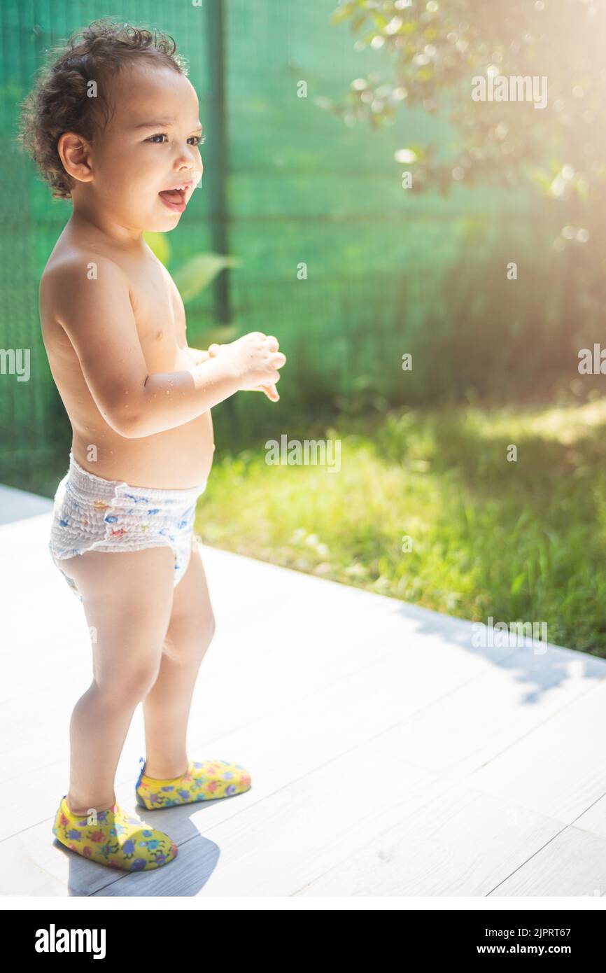 Glücklich lockig Kleinkind Junge in Windel spielen im Hinterhof in der Sonne Stockfoto