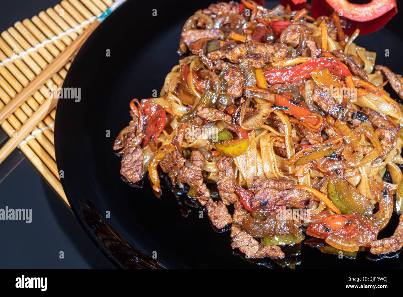 Udon-Nudeln mit Fleisch, Pilzen und Gemüse. Mit Sesamsamen bestreut. Asiatische Lebensmittel, Braten auf schwarzem Hintergrund, Kopierraum Stockfoto