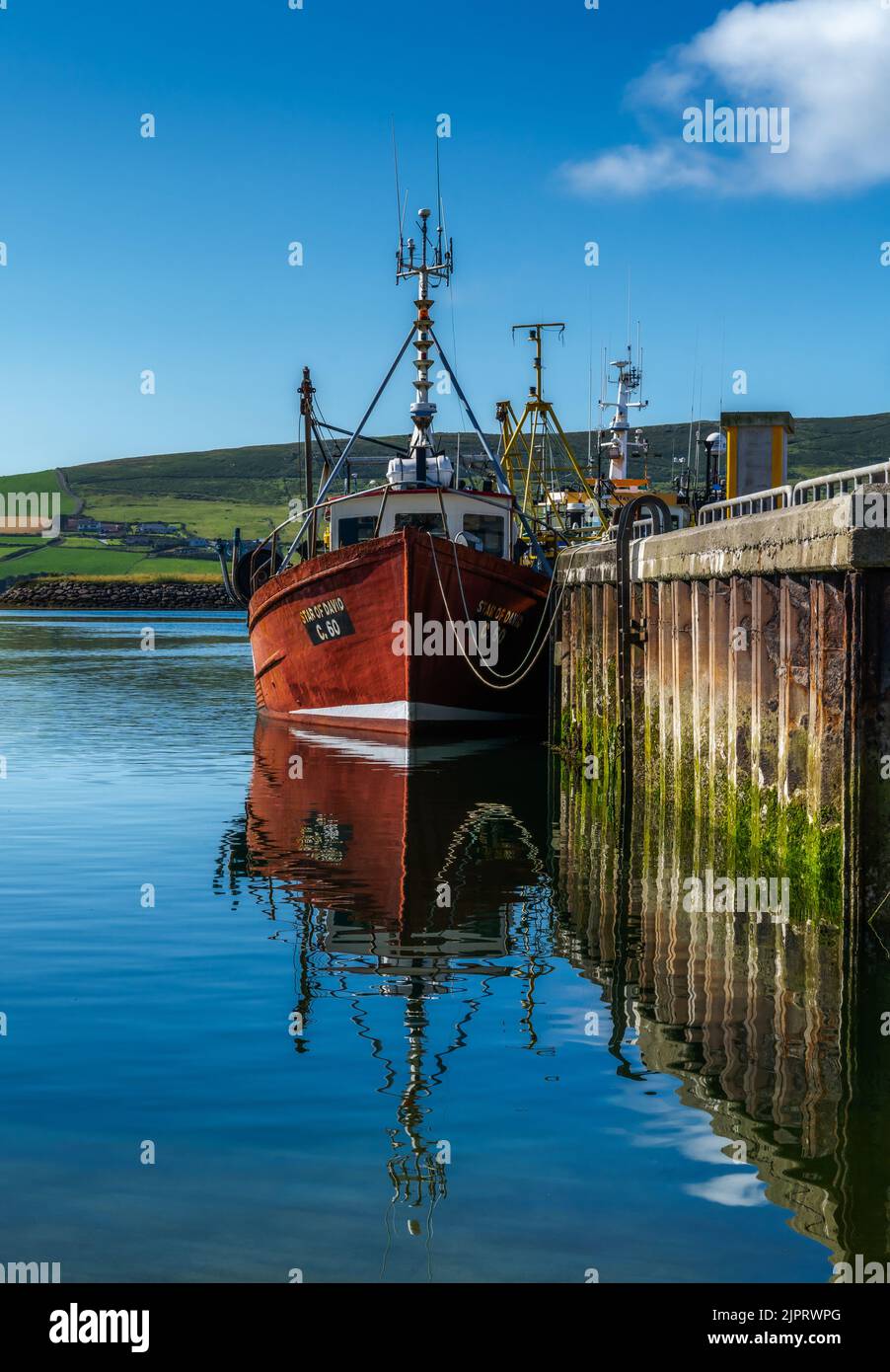Dingle, Irland - 7. August 2022: Rotes Fischerboot auf den Docks von Dingle Harbour in der Grafschaft Kerry mit Reflexionen im ruhigen Wasser Stockfoto
