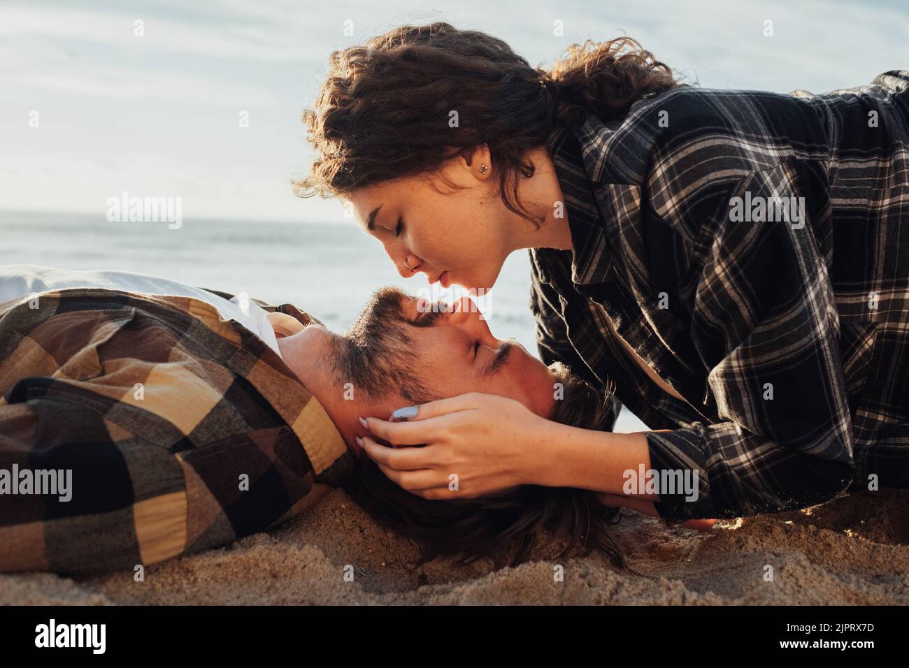 Junges erwachsenes Paar, das am Strand des Meeres liegt, kaukasische lockige Frau, die ihren Freund küsst Stockfoto