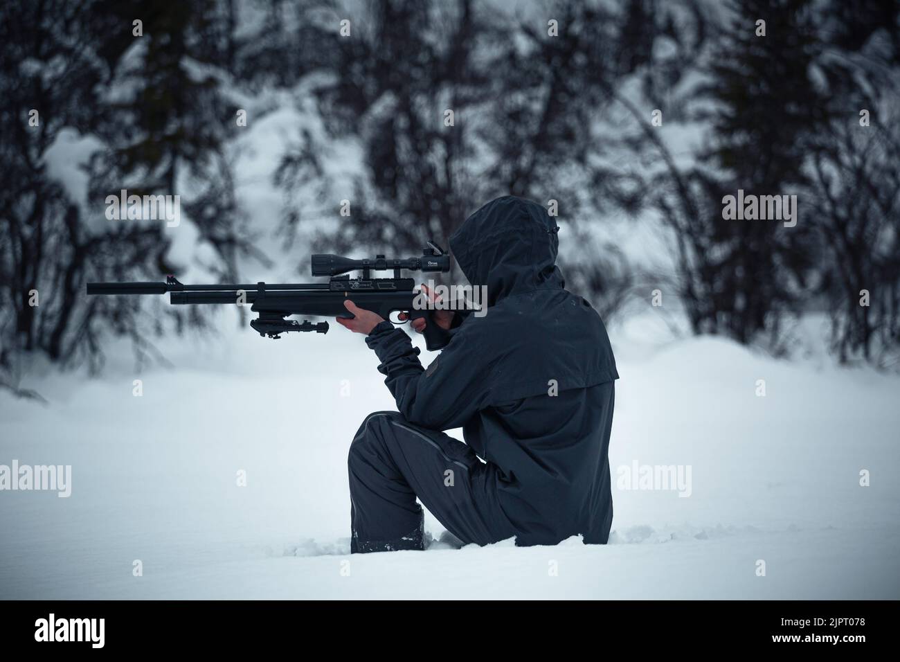 Ein Mann, der im Winter ein Gewehr hält und in einem Wald anvisier Stockfoto