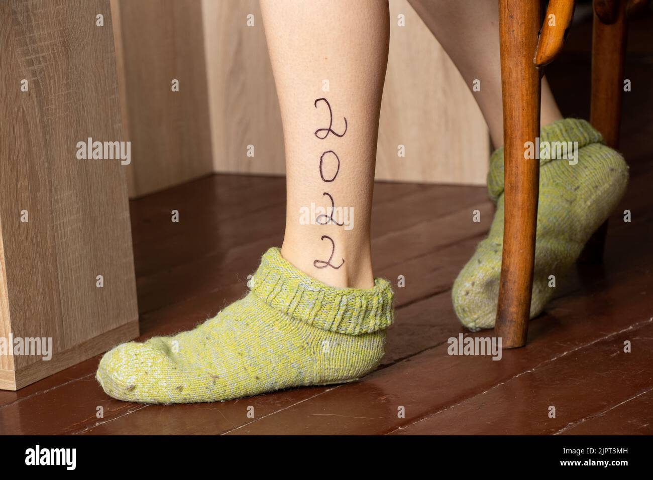 2022 geschrieben auf dem Bein eines Mädchens, das an einem Tisch auf dem Holzboden eines Hauses sitzt, glückliches neues Jahr 2022 Stockfoto