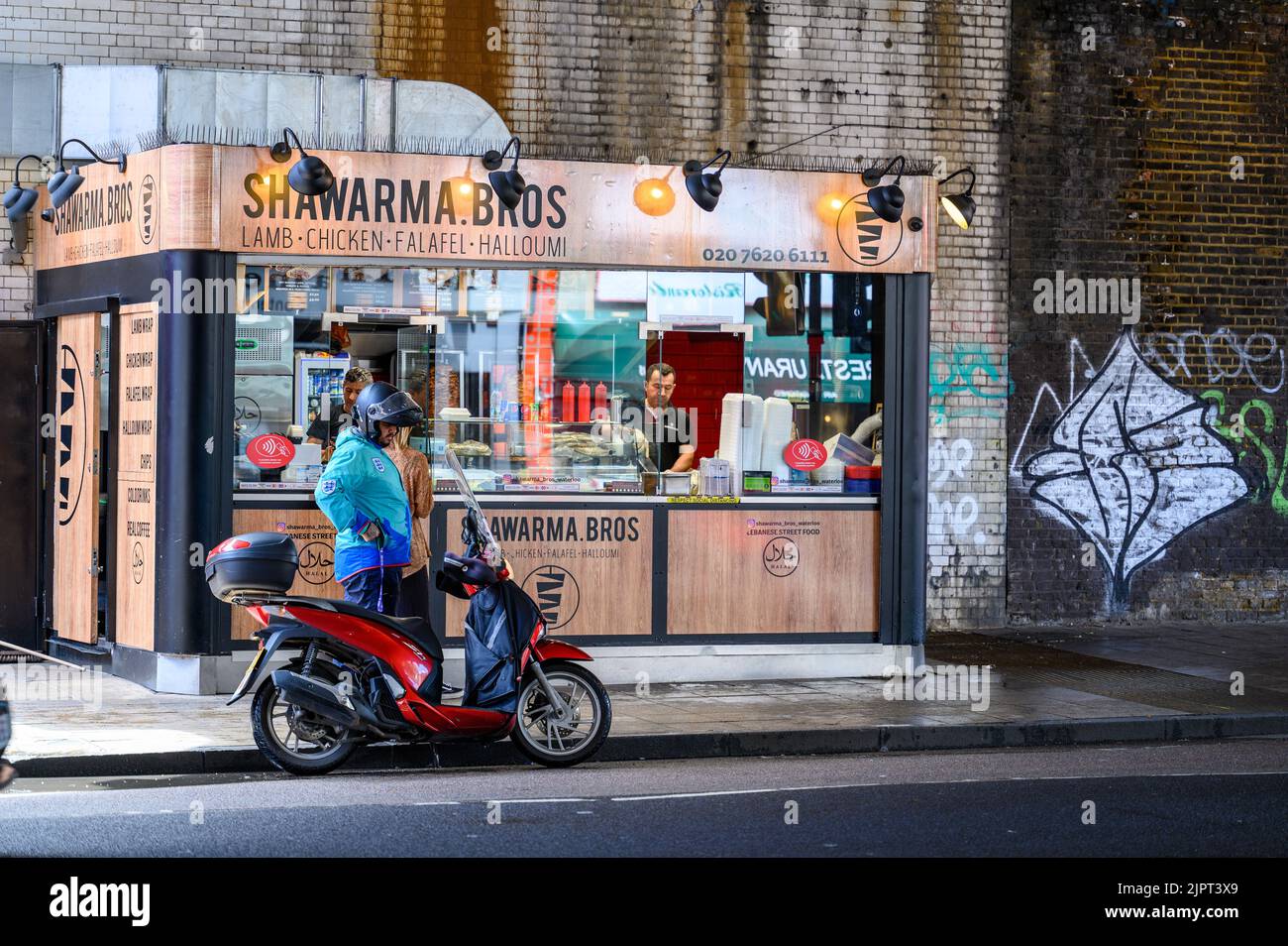 LONDON - 20. Mai 2022: Lebensmittelzulieferer und Motorroller vor dem Lebensmittelkioské im Nahen Osten unter der Eisenbahnbrücke in der Nähe der Waterloo Station Stockfoto