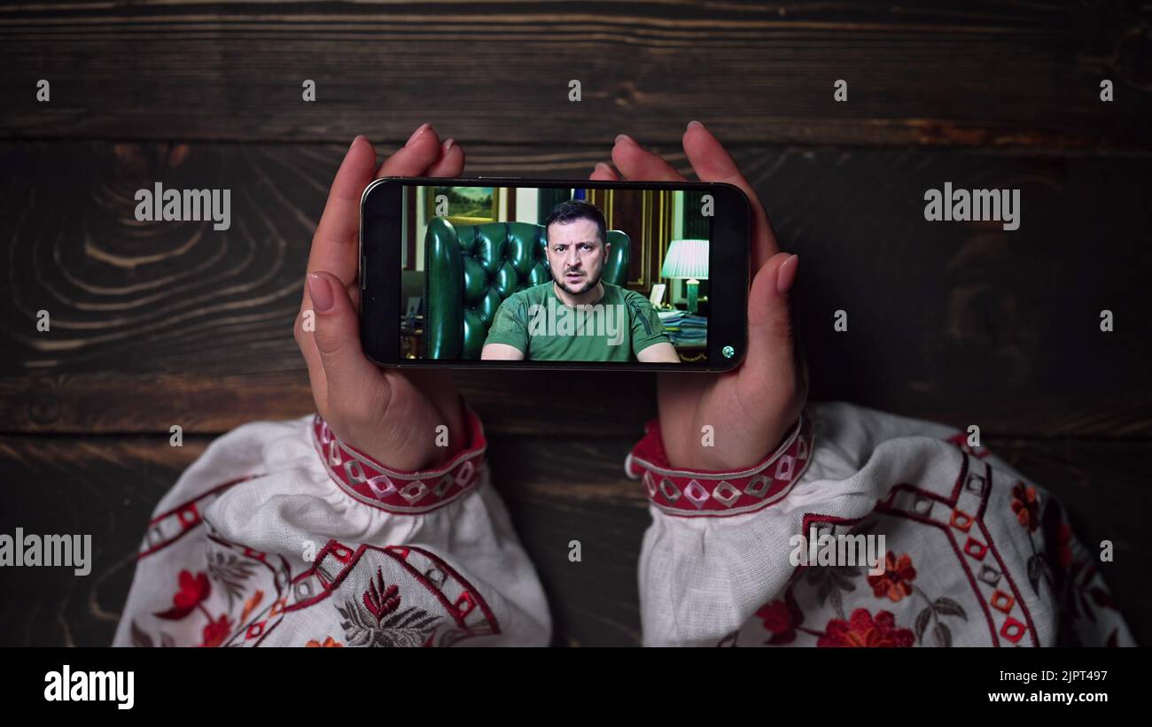 August 2022 - Kiew, Ukraine. Online-Rede von Präsident Volodymyr Zelenskiy auf dem Smartphone auf Holztisch Hintergrund beobachten. Nachrichten von vorne Stockfoto