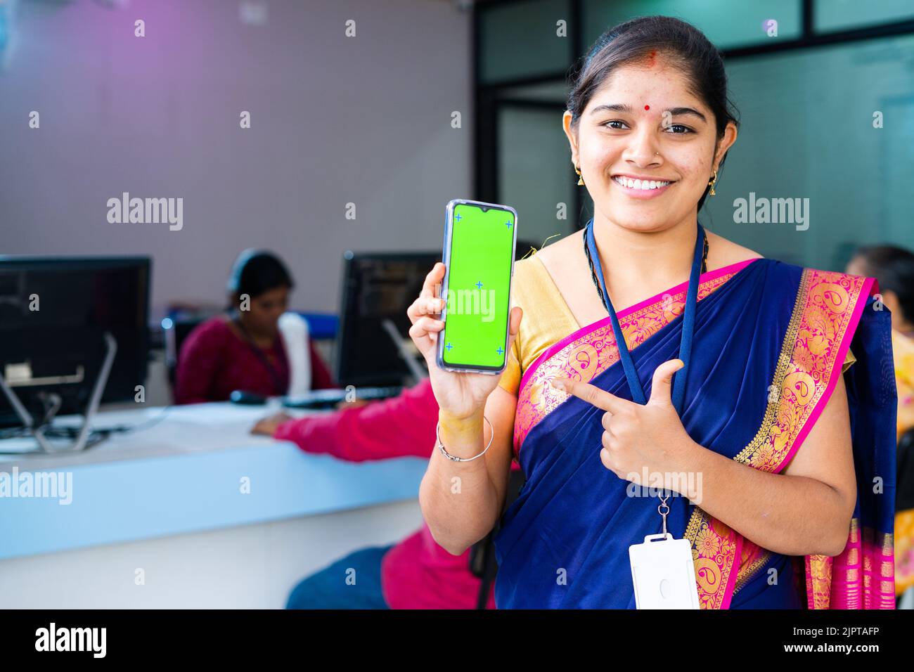 Lächelnde Frau Bankangestellte zeigt grünen Bildschirm Handy durch Zeigen mit dem Finger durch die Kamera - Konzept der Online-Finanzdienstleistungen Stockfoto