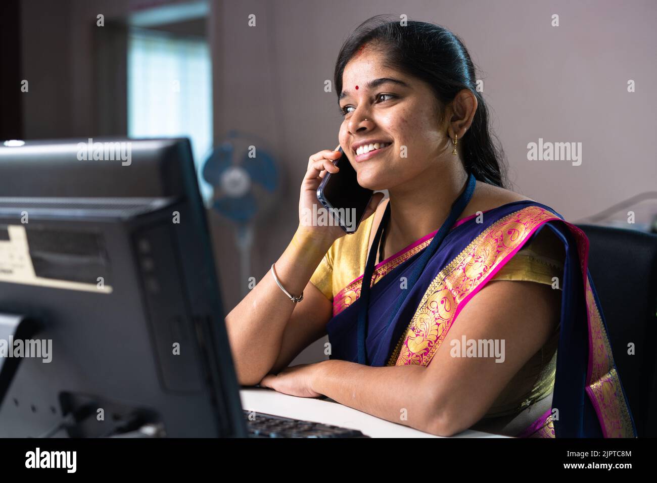 Ein glücklicher, lächelnder Banker, der mit dem Kunden auf dem Mobiltelefon spricht, während er bei der Bank sitzt – Konzept der Kommunikation, des Finanzberaters und der Entspannung. Stockfoto