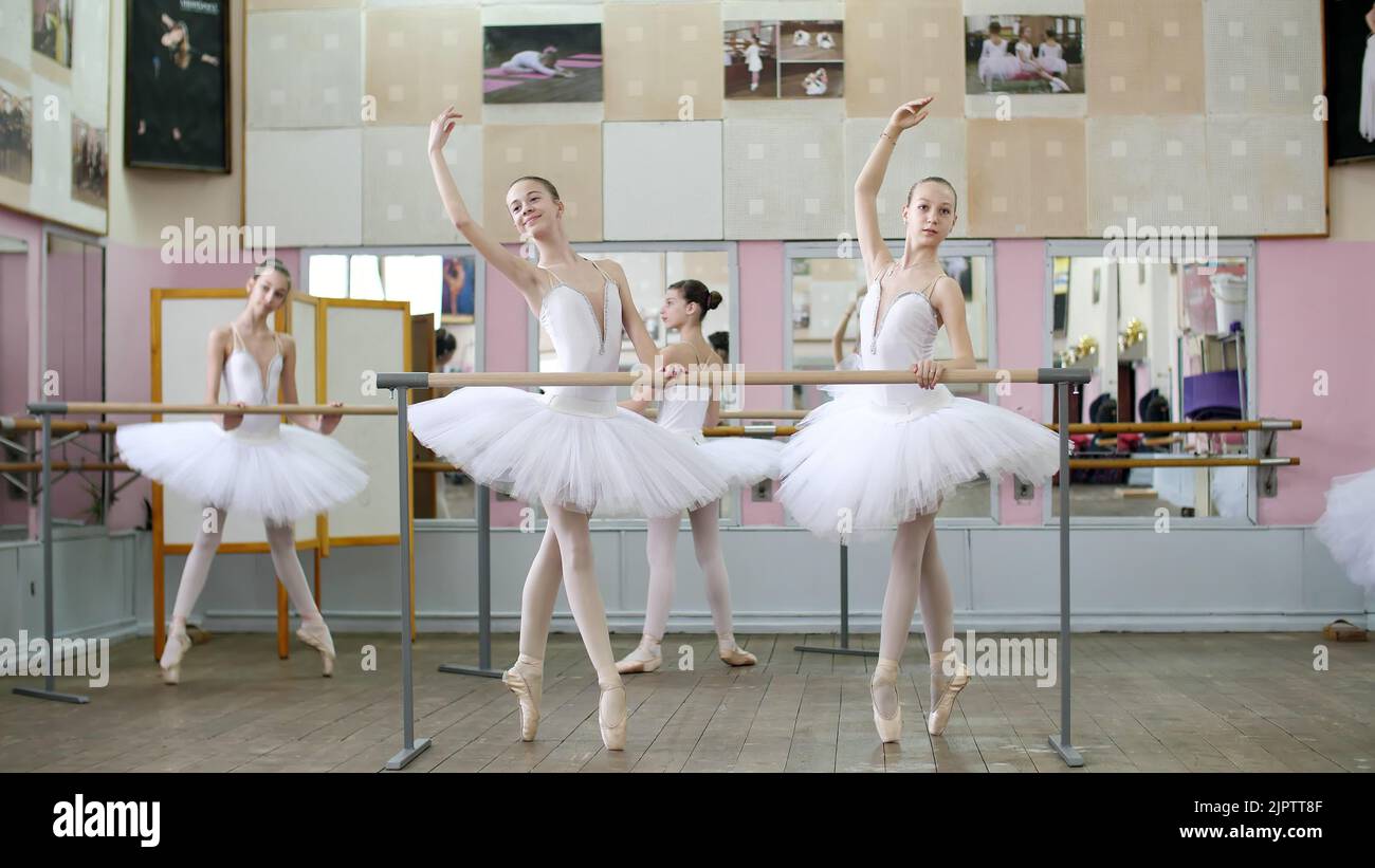 Im Ballettsaal werden Mädchen in weißem Balletttutus, Packs beim Ballett verlobt, Proben croise Forward, Junge Ballerinas, die in Spitzenschuhen am Geländer im Ballettsaal auf den Zehen stehen. Hochwertige Fotos Stockfoto