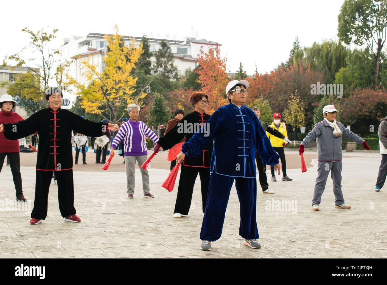 Chinesische Senioren üben Tai Chi mit Kung Fu Fans am frühen Morgen auf dem Stadtplatz von Lijiang. Stockfoto