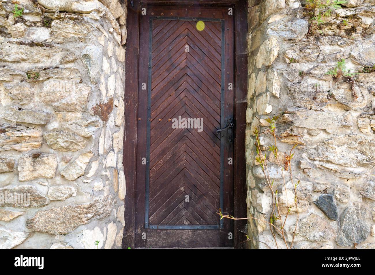 Nahaufnahme einer dunklen Holztür in einer Wand aus unterschiedlich großen Kalksteinfelsen Stockfoto