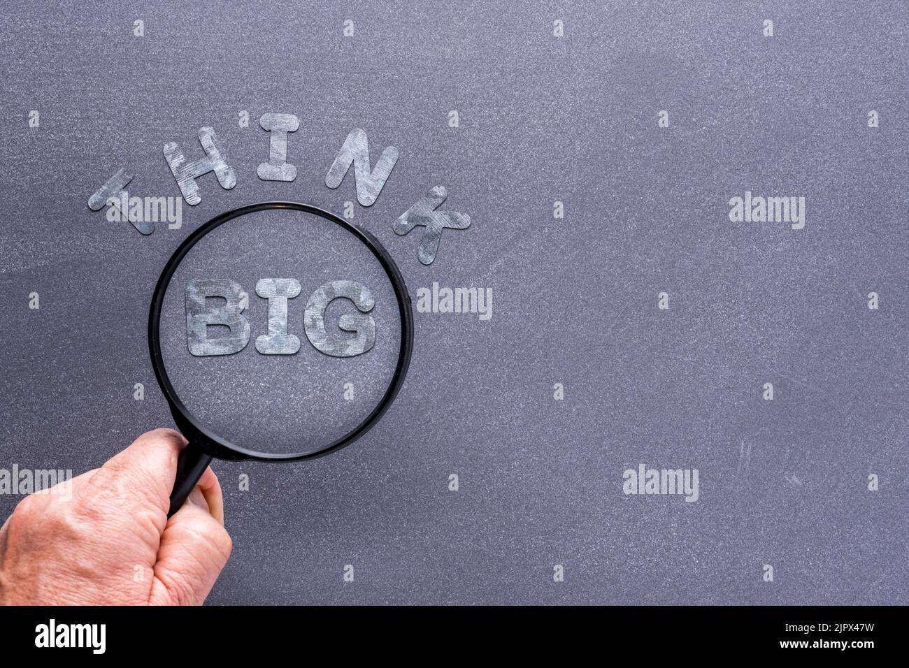 Think Big Konzept mit Kreidetafel Hintergrund und Hand halten Lupe über verzinkten Buchstaben Stockfoto