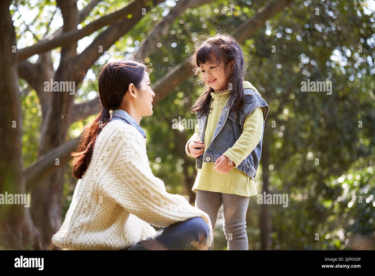 Junge asiatische Mutter sitzt auf Gras im Park mit einem angenehmen Gespräch mit niedlichen Tochter Stockfoto