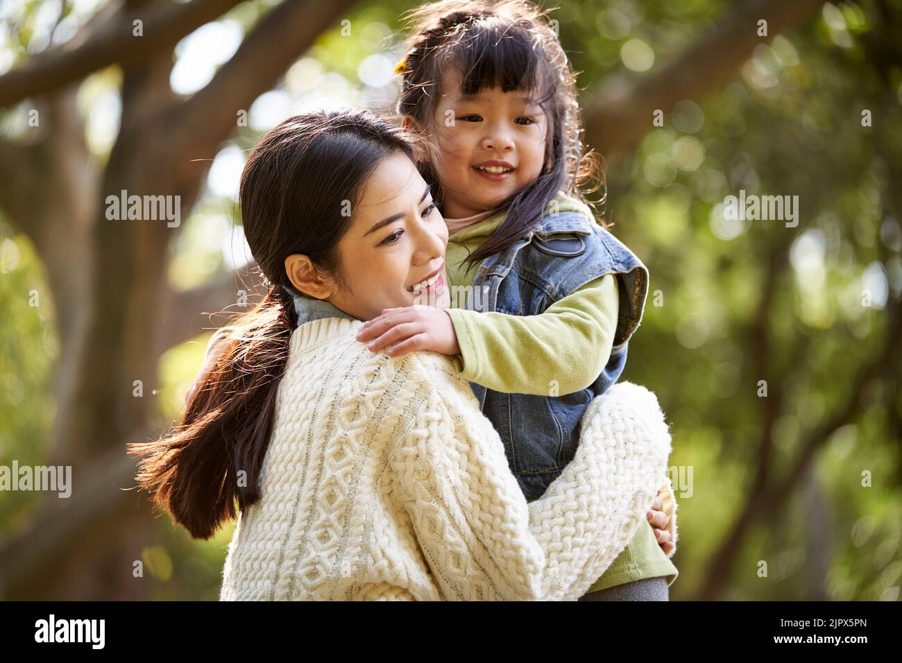 Liebevolle asiatische Mutter umarmt niedlich Tochter im Freien im Park glücklich und lächelnd Stockfoto